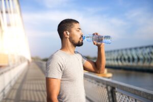 Athletic man drinking bottled water on a bridge after a run.