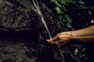 A woman's hands cupping a stream of water flowing from a rock.