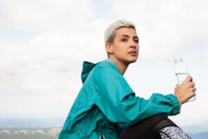 Hiker wearing a teal windbreaker and holding a bottled water.