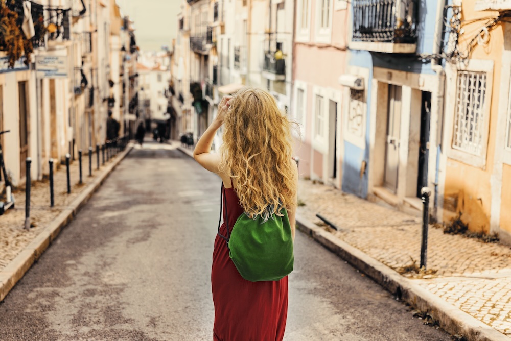 A young female tourist in a red dress walking down an empty city street.