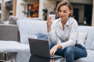 Young mom enjoying a glass of water while working on a computer