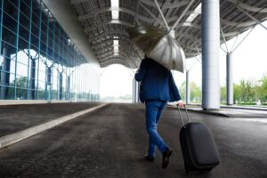 A young businessman holding suitcase and umbrella walking in rain