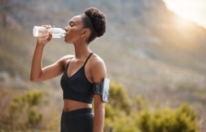 Female runner drinking bottled water in front of a mountain landscape.