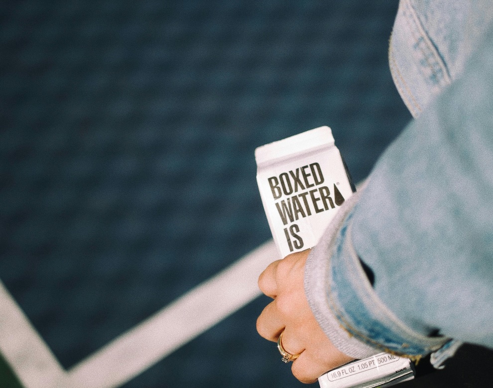 Person wearing a denim jacket and carrying boxed water.