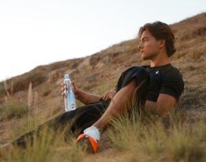 Athlete reclining on a hill holding a one water bottle.