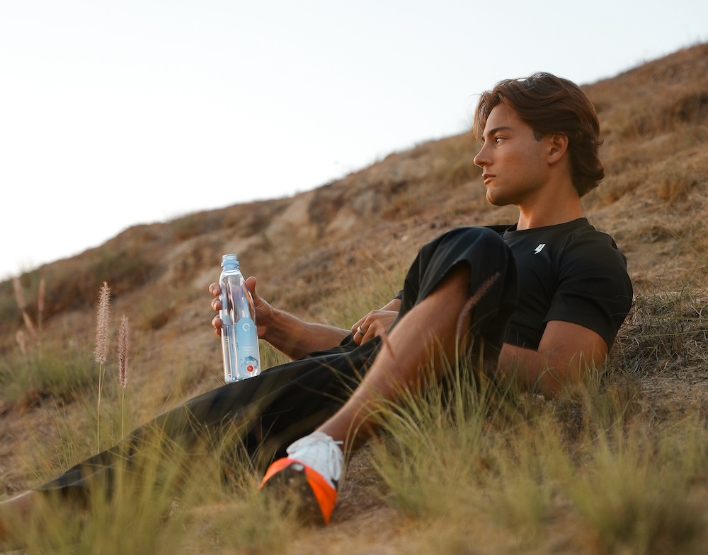 Athlete reclining on a hill holding a one water bottle.