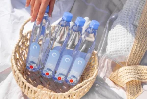 A woman's hand removing a One Water bottle from a wicker basket.