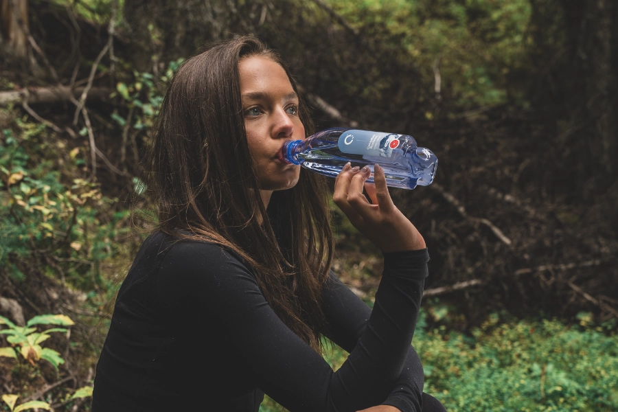 Woman drinking One Water while sitting on the forest floor.