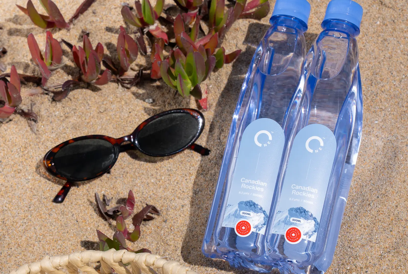 Interlocked One Water bottles laying on the beach with sunglasses.