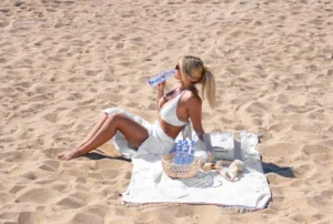 Woman drinking One Water on a beach.