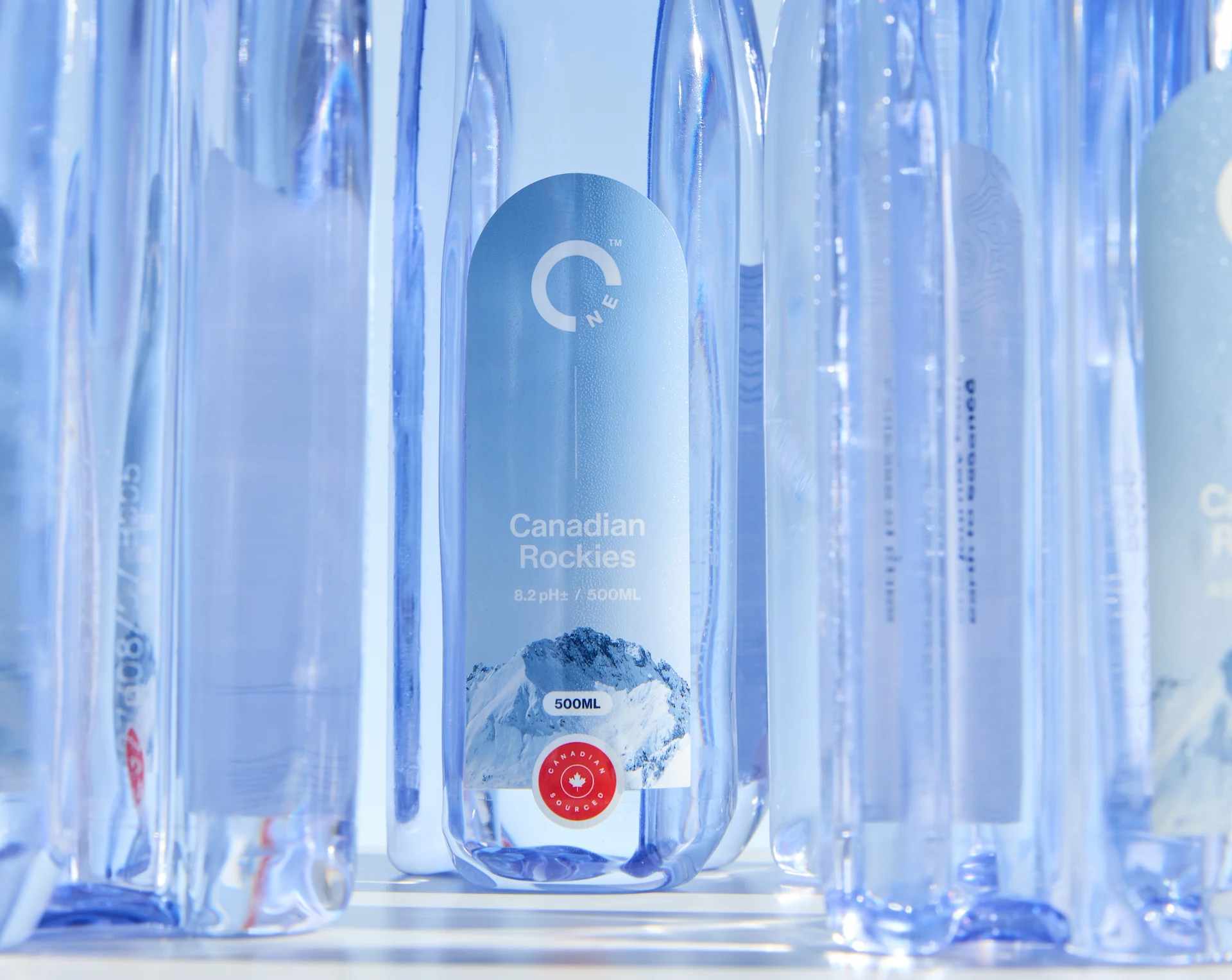 Closeup of a forward-facing One Water bottle in between rear-facing bottles.
