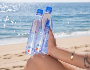 Woman holding interlocked One Water plastic bottles on the beach.