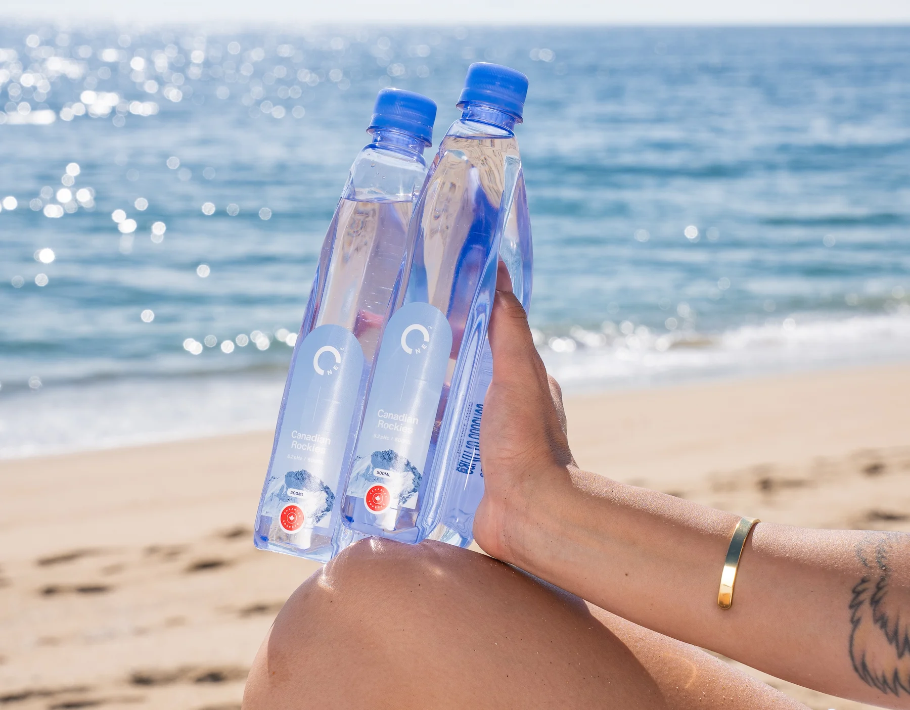 Woman holding interlocked One Water plastic bottles on the beach.