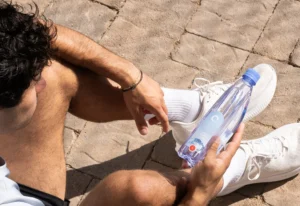 Man in athletic wear sitting on the ground and holding a One Water bottle.